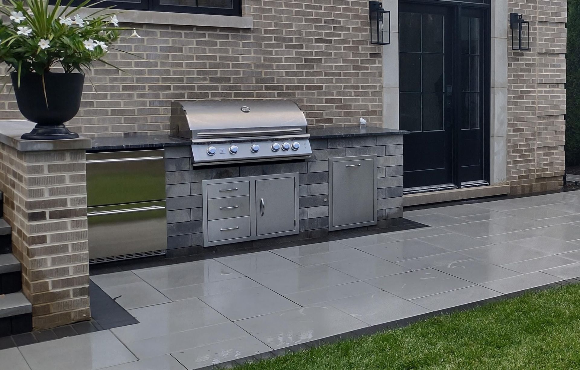 Outdoor kitchen with grill, stainless steel appliances, and brick/stone façade.