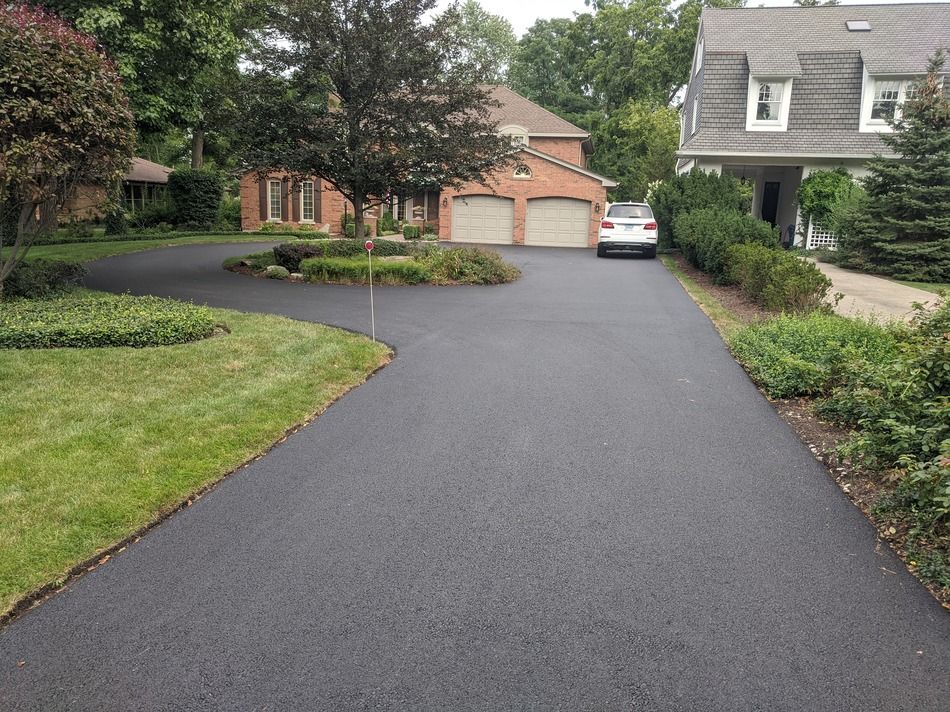 Black asphalt driveway leading to brick house with two-car garage. Car parked on driveway.