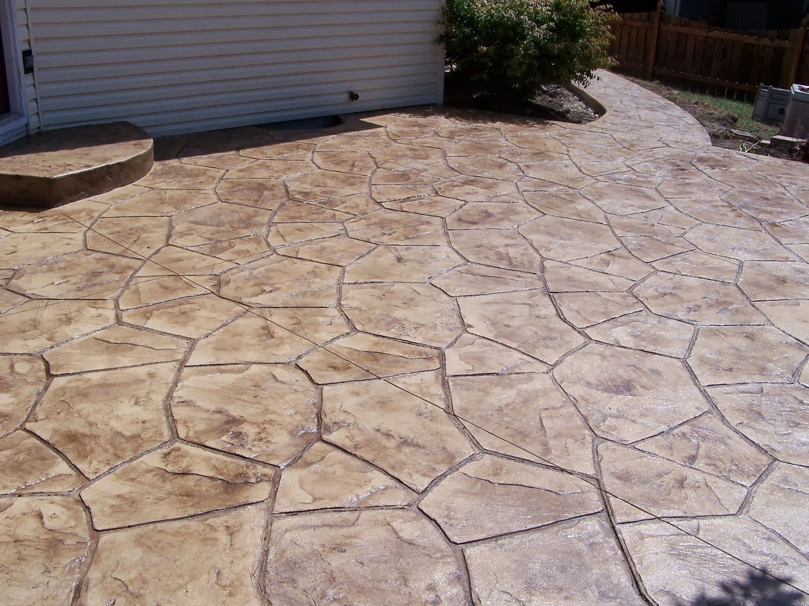Stamped concrete patio with a stone-like pattern, in brown and gray hues, leading to a pathway and a building in Naperville, IL.