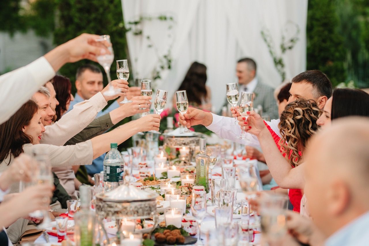 Guests raise glasses at a long banquet table during a celebratory indoor dinner