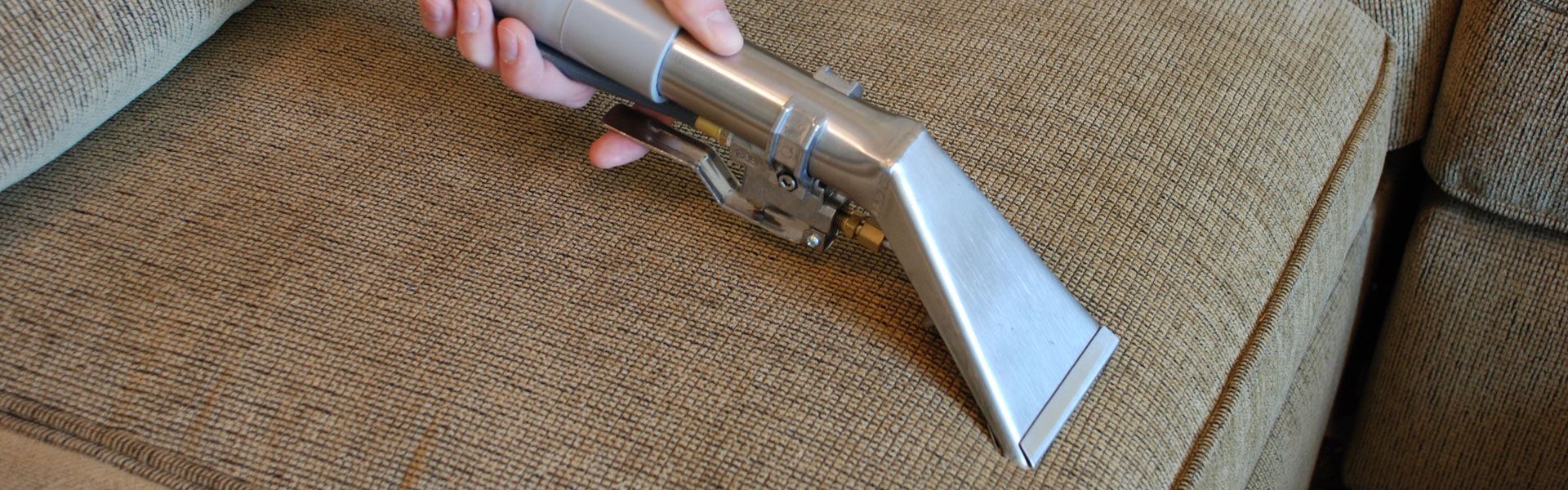 A person is cleaning a couch with a vacuum cleaner.