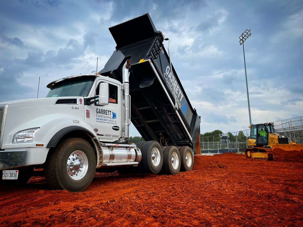 Red dump truck hauling soil on a red dirt construction site under a clear sky
