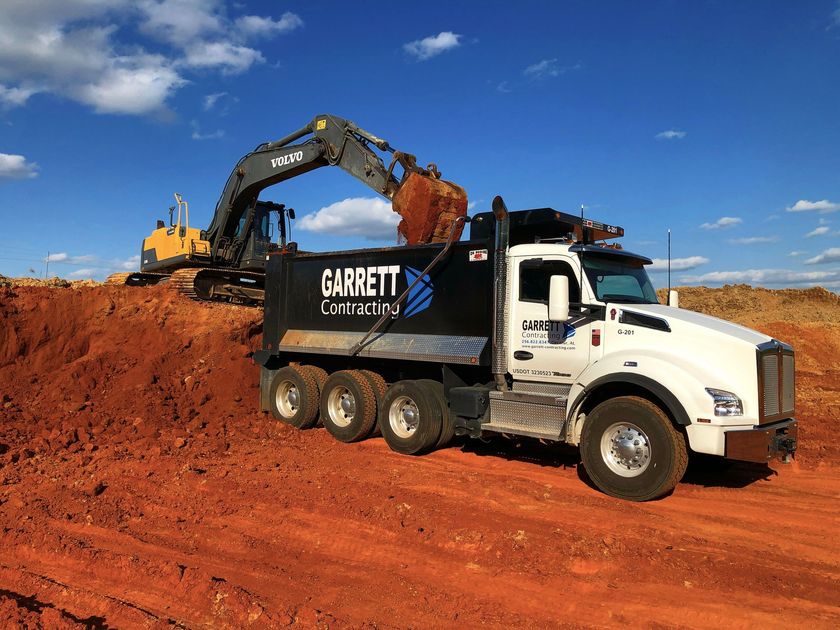 Bulldozer and excavator on a red dirt construction site under clear sky