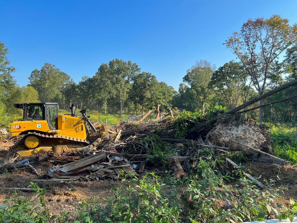 Construction vehicles grading a red dirt road in a green rural landscape