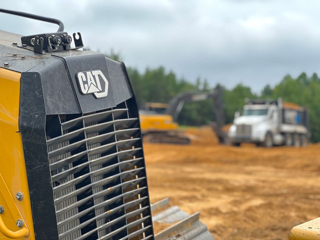 Yellow excavators and dump trucks working on a red dirt construction site.