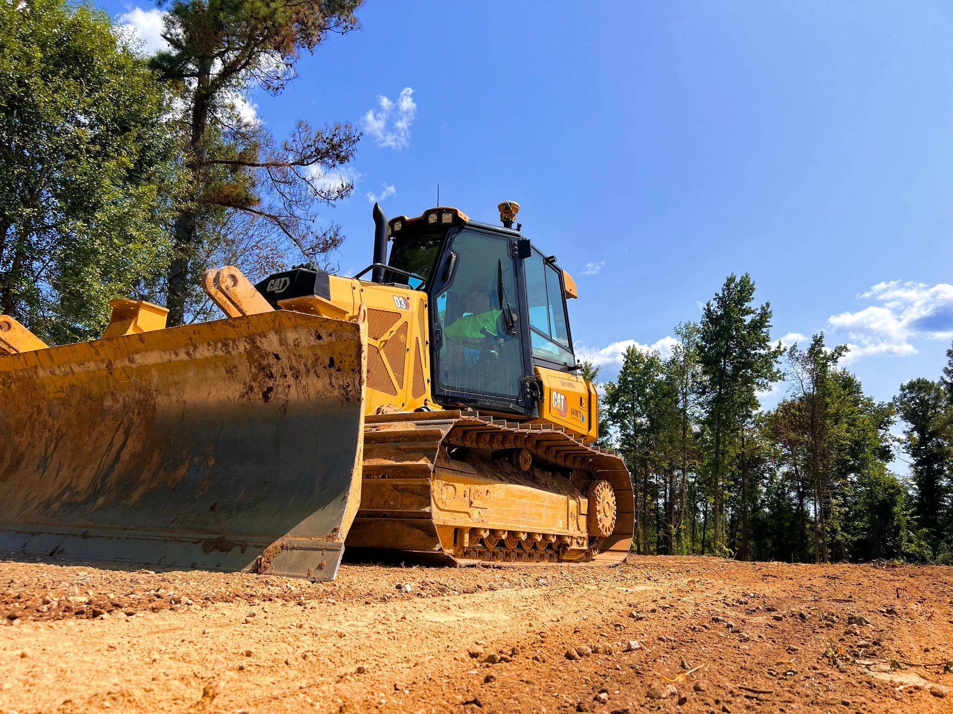 Yellow road grader on red dirt field with trees in the background Yellow road grader on red dirt field with trees in the background