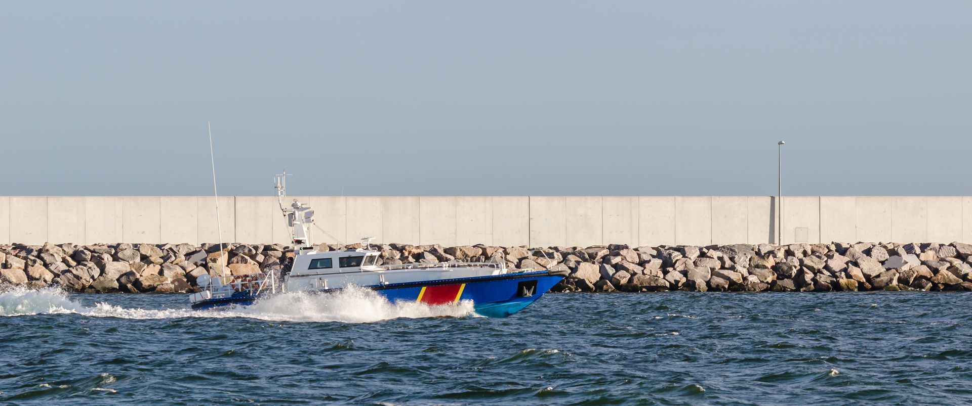 A speedboat water near a rocky breakwater and concrete seawall. A speedboat water near a rocky breakwater and concrete seawall.