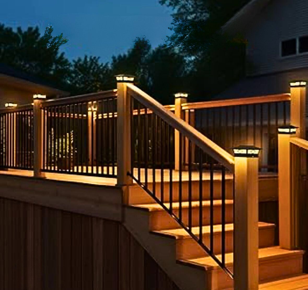 Wooden deck with black railings and stair lights illuminated at dusk.