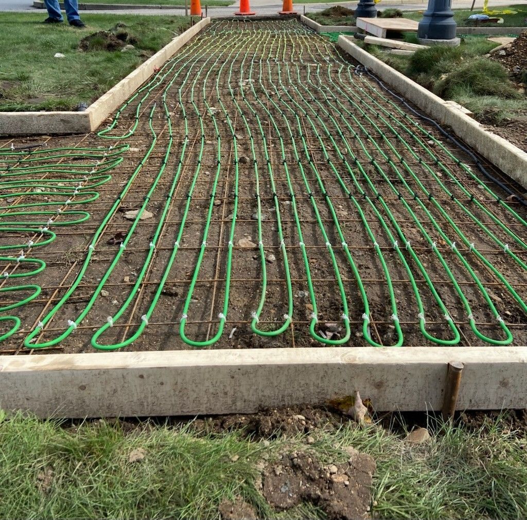 Green heating tubes laid on a wire grid within a concrete walkway frame, ready for concrete pouring.