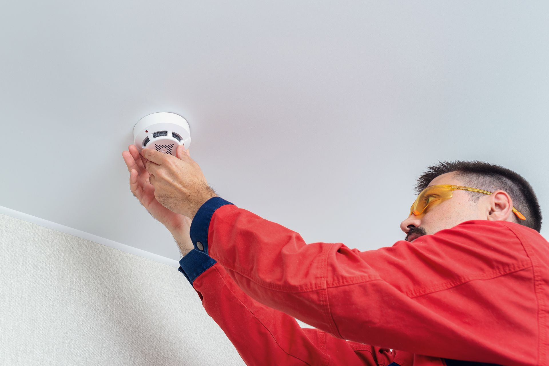 Worker installing fire alarm or smoke detector on the ceiling.