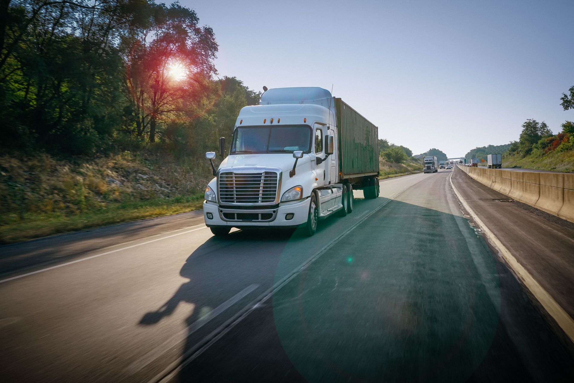 White semi-truck hauling a trailer on a sunny highway; trees line the roadside.