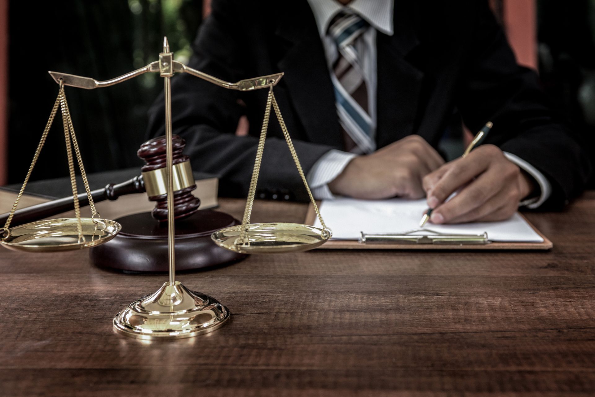 A man in a suit and tie is writing on a clipboard next to a scale of justice.