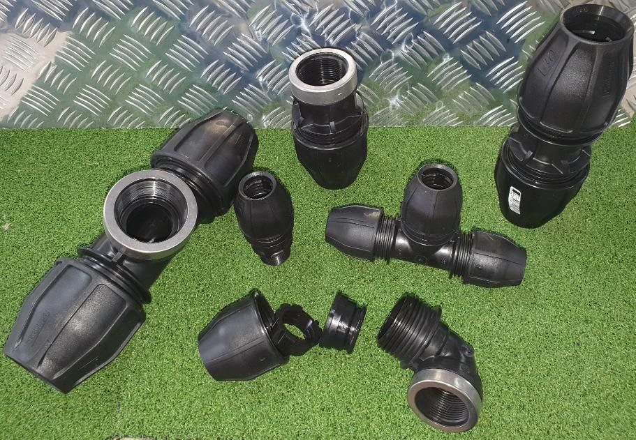 A Bunch of Black Plastic Pipe Fittings Are Sitting on The Grass — Peel Irrigation & Water Supplies in Taminda, NSW