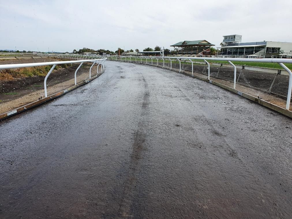 A Muddy Road with A White Railing and A Building in The Background — Peel Irrigation & Water Supplies in Taminda, NSW