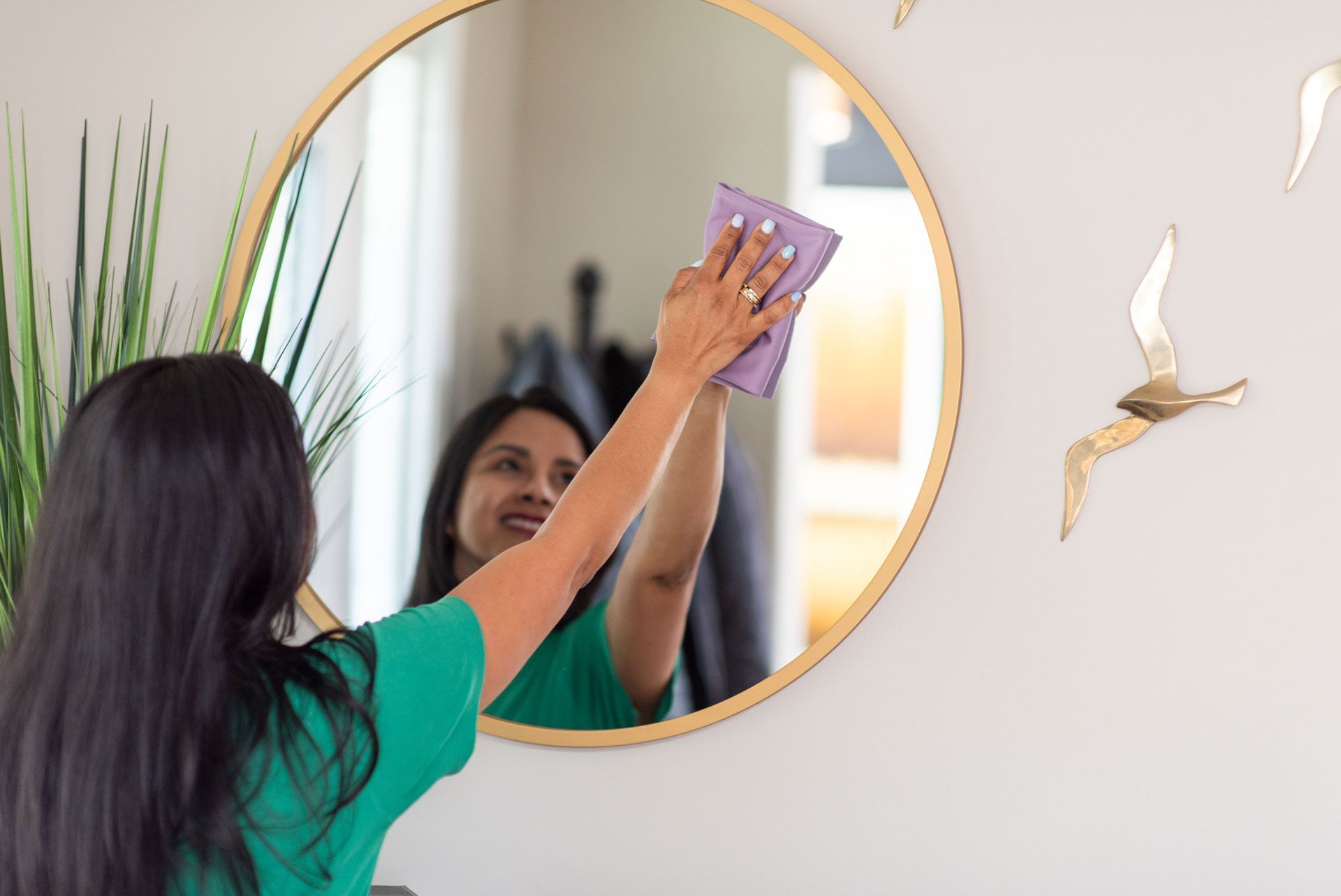 Woman cleaning a round wall mirror with a cloth in a bright room
