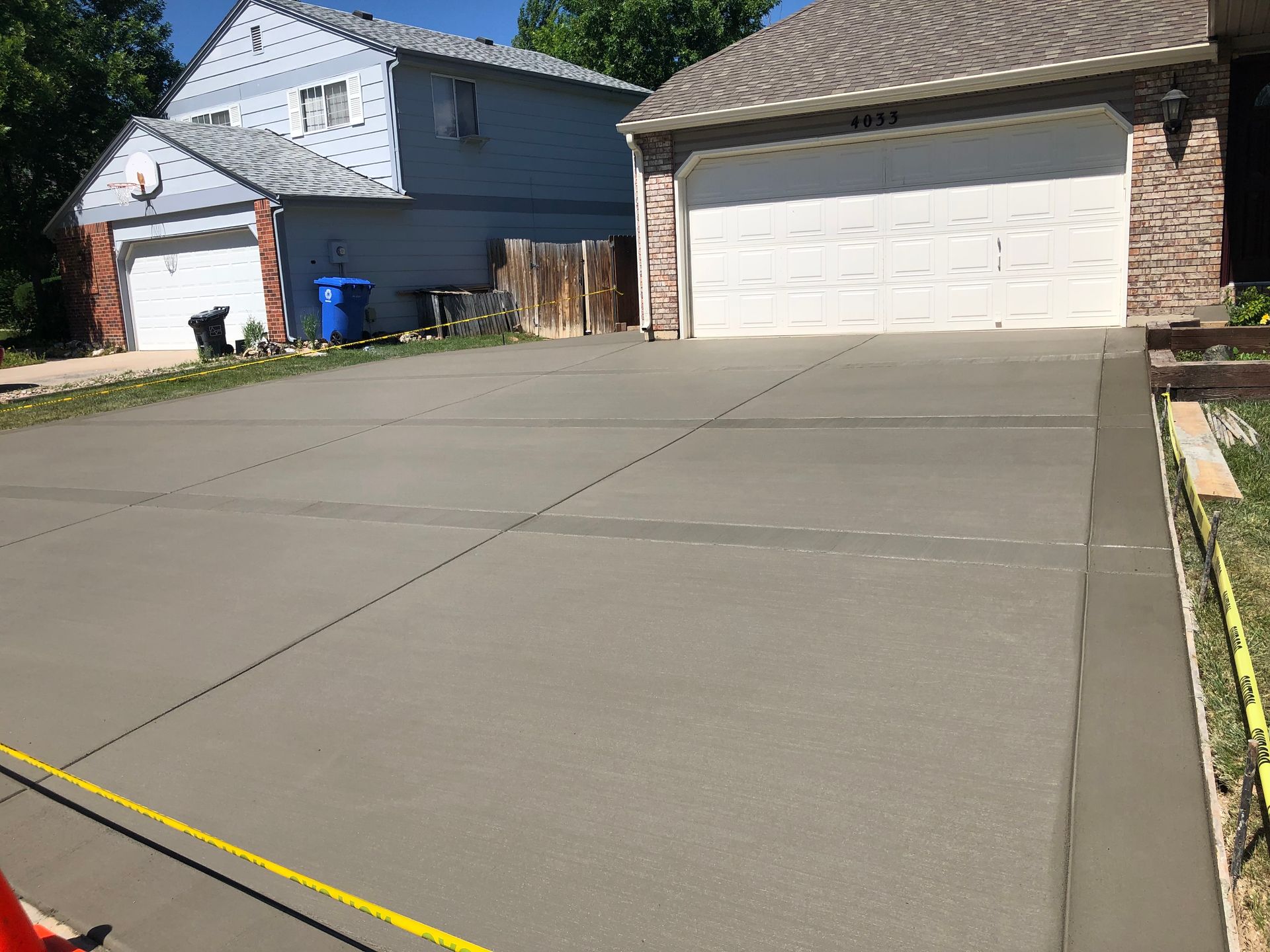 Two suburban houses with a large freshly poured concrete driveway under a clear sky