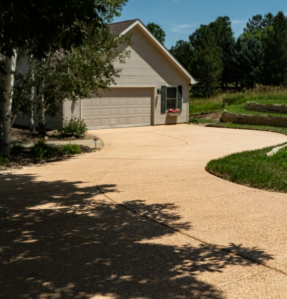 Suburban driveway leading to a beige garage beside a landscaped yard on a sunny day