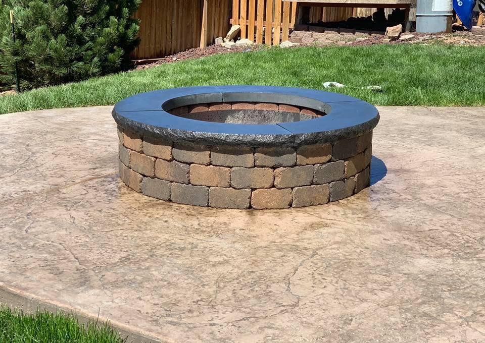 Circular stone fire pit with black rim on a concrete patio in a backyard