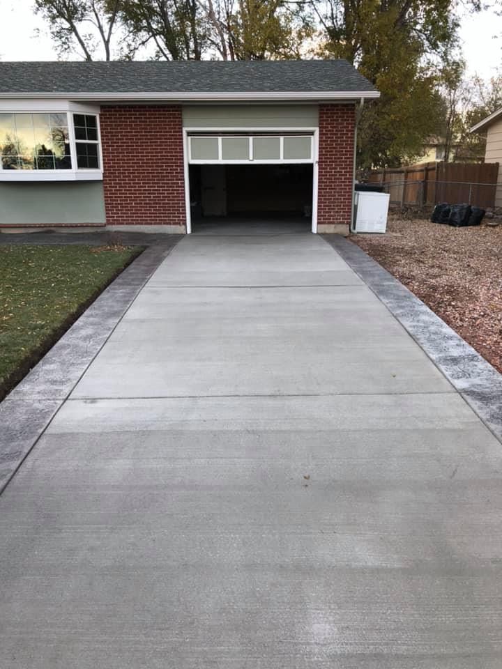 Concrete driveway leading to an open garage on a brick house, bordered by grass and gravel.