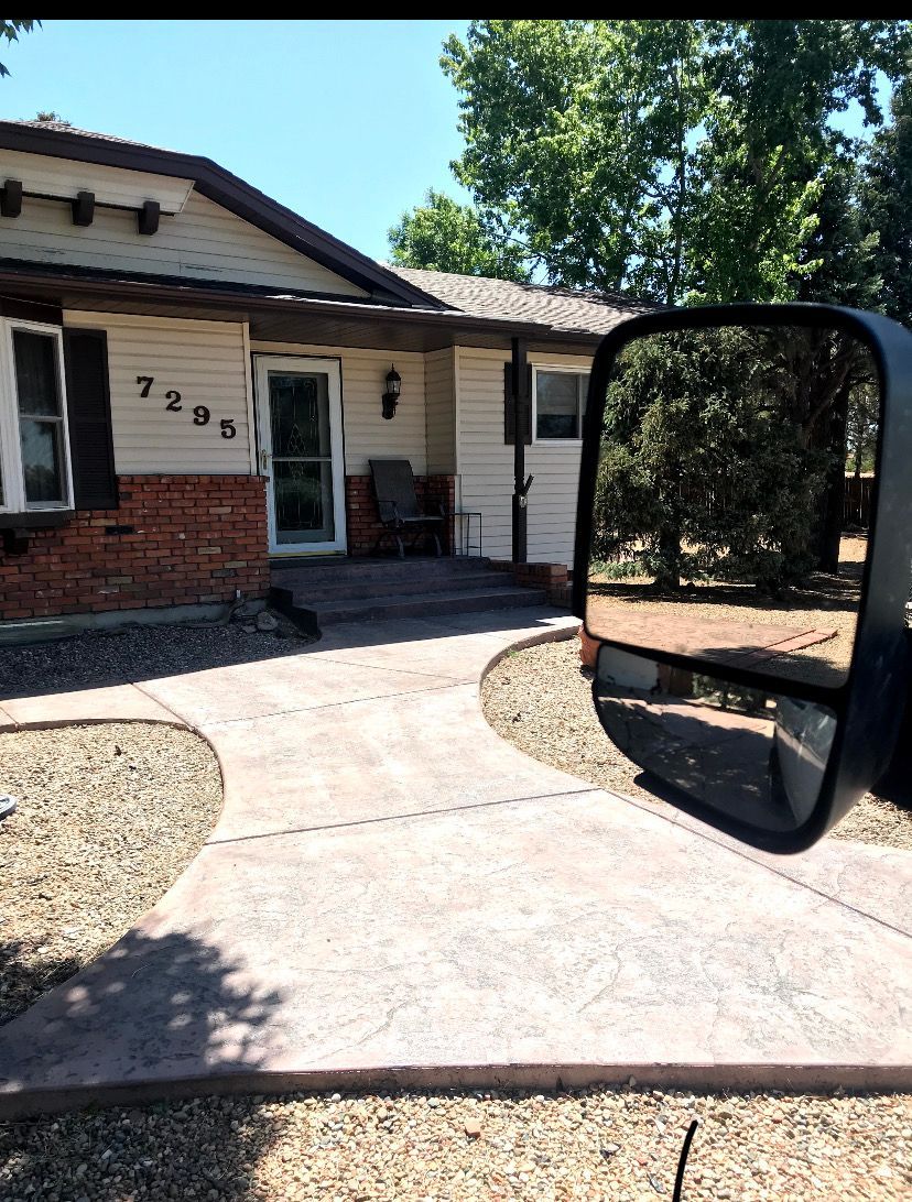 Front entrance of a house with a curved concrete driveway and a vehicle side mirror in the foreground.
