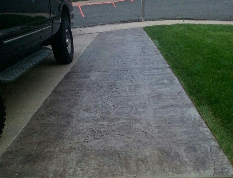 Concrete driveway beside a parked black vehicle and green lawn