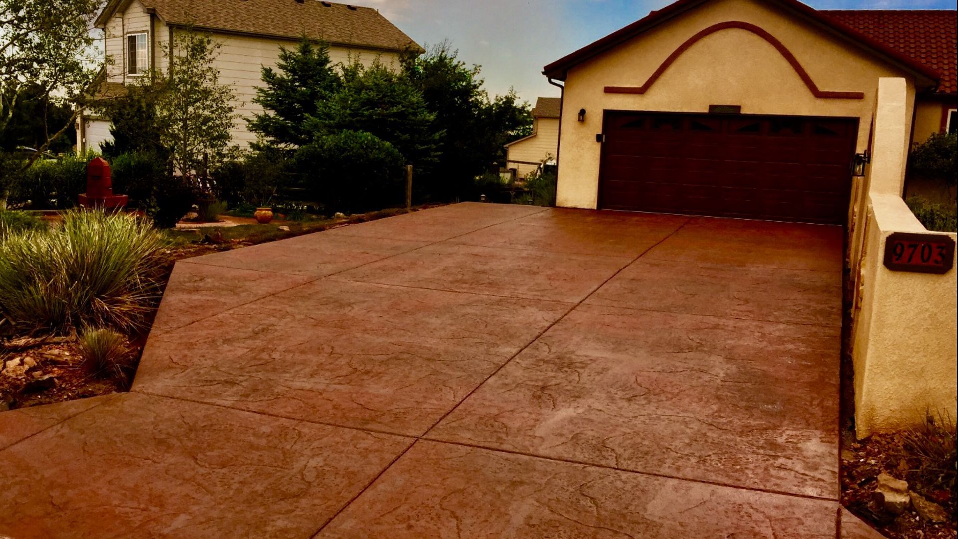 Wide concrete driveway leading to a beige garage with dark brown doors beside a landscaped house