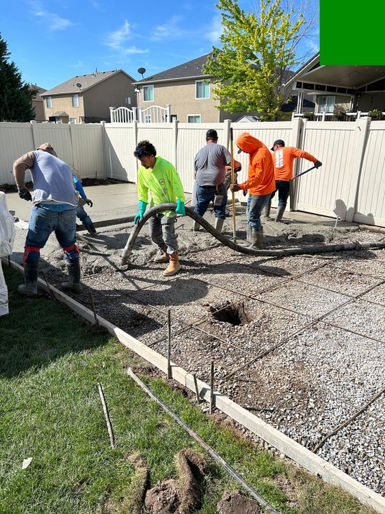 Workers in neon vests leveling gravel in a fenced backyard on a sunny day