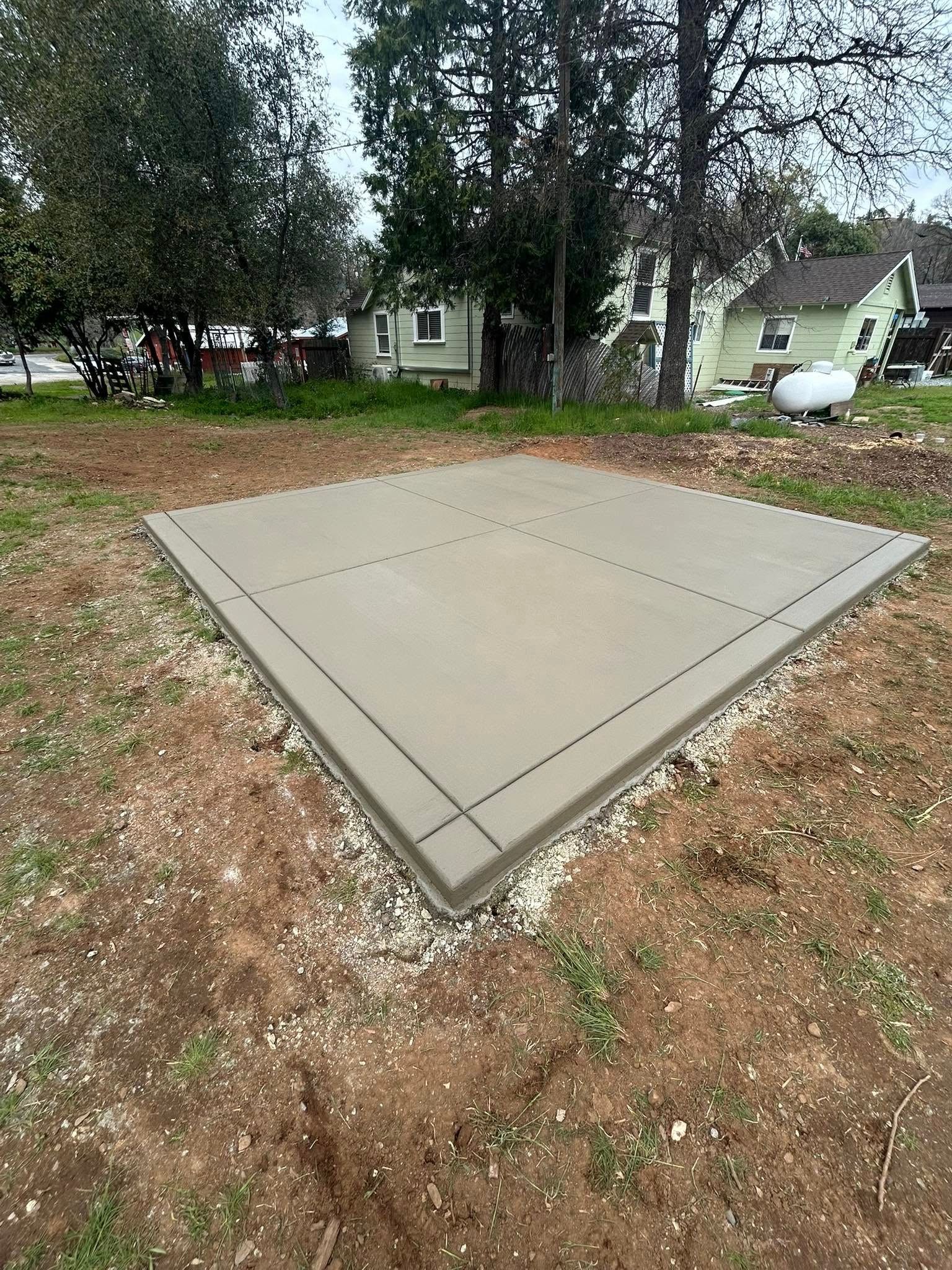 Concrete pad in a wooded yard with a small house in the background