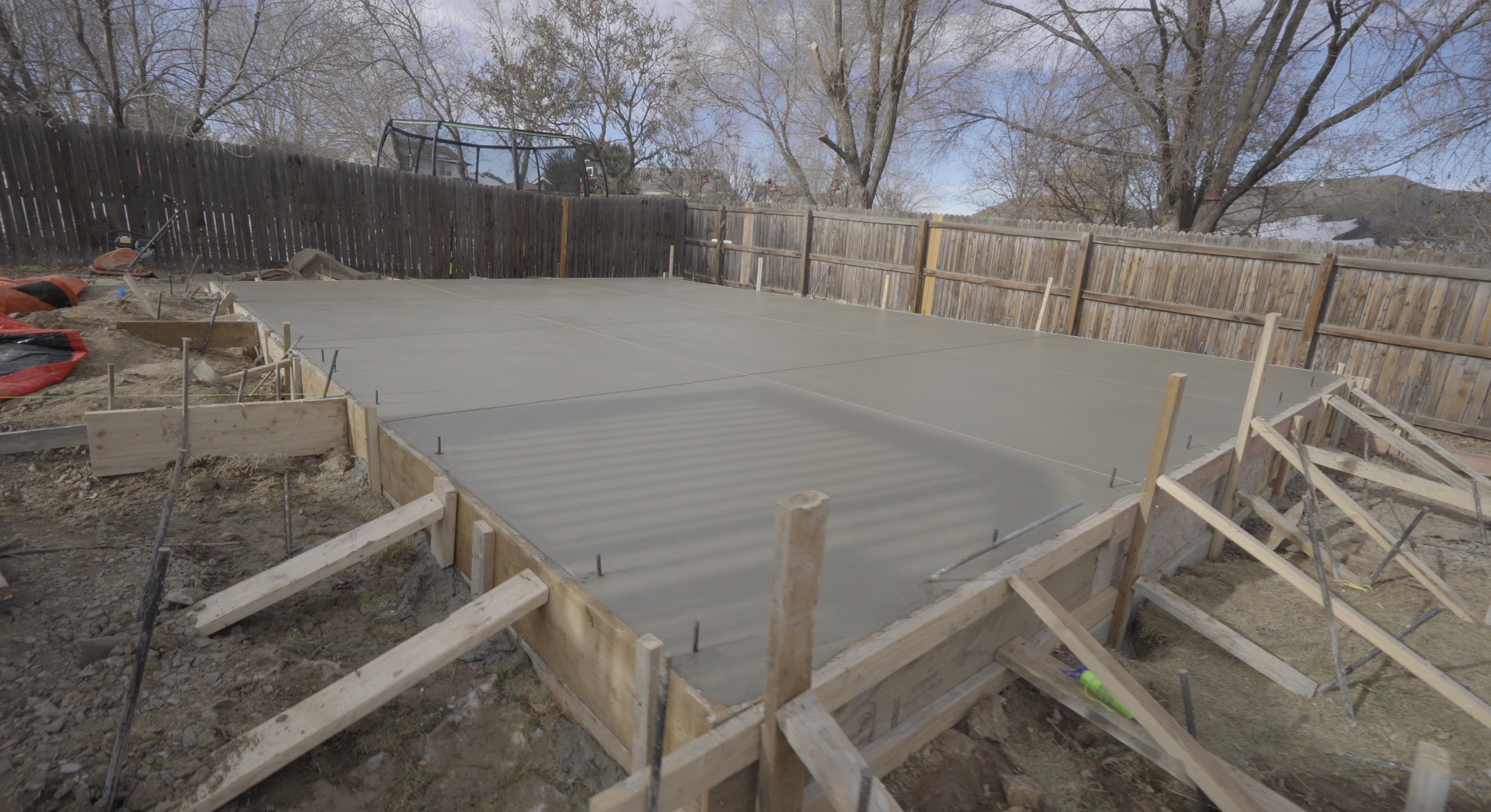 Freshly poured concrete slab framed by wooden forms in a fenced backyard during construction