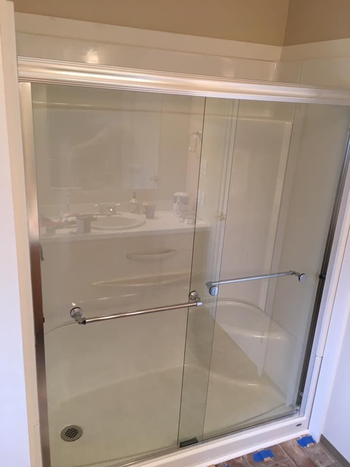 White-walled shower stall with sliding glass doors, chrome hardware, and a small built-in seat.