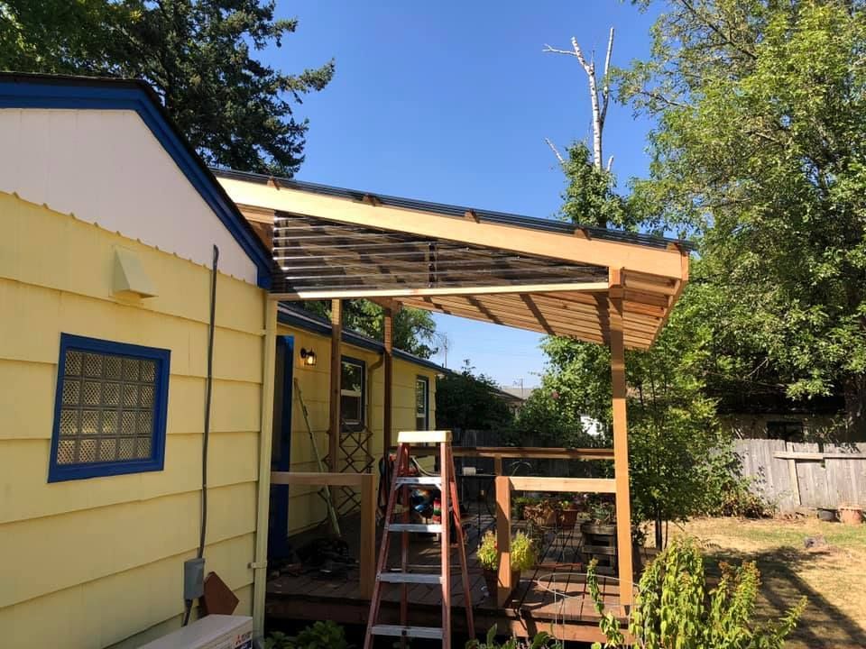 Yellow house with wooden deck and a pergola-style roof extending over it. A ladder is present.