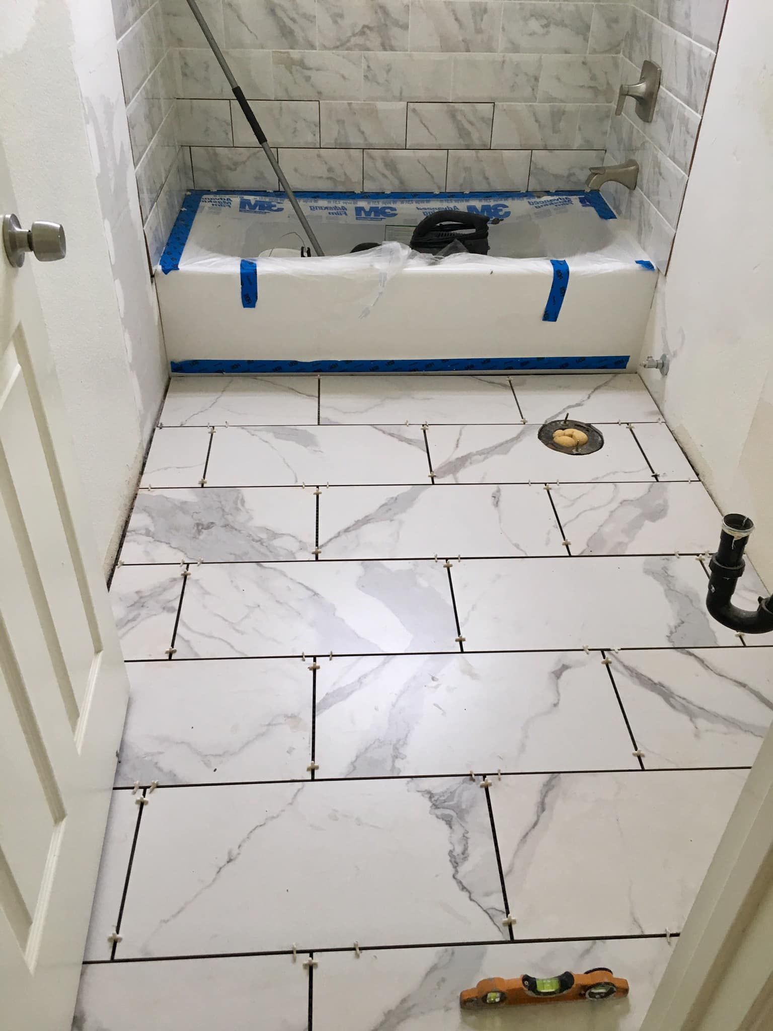 Bathroom with marble-look tile flooring and walls, a white bathtub, and construction tools.
