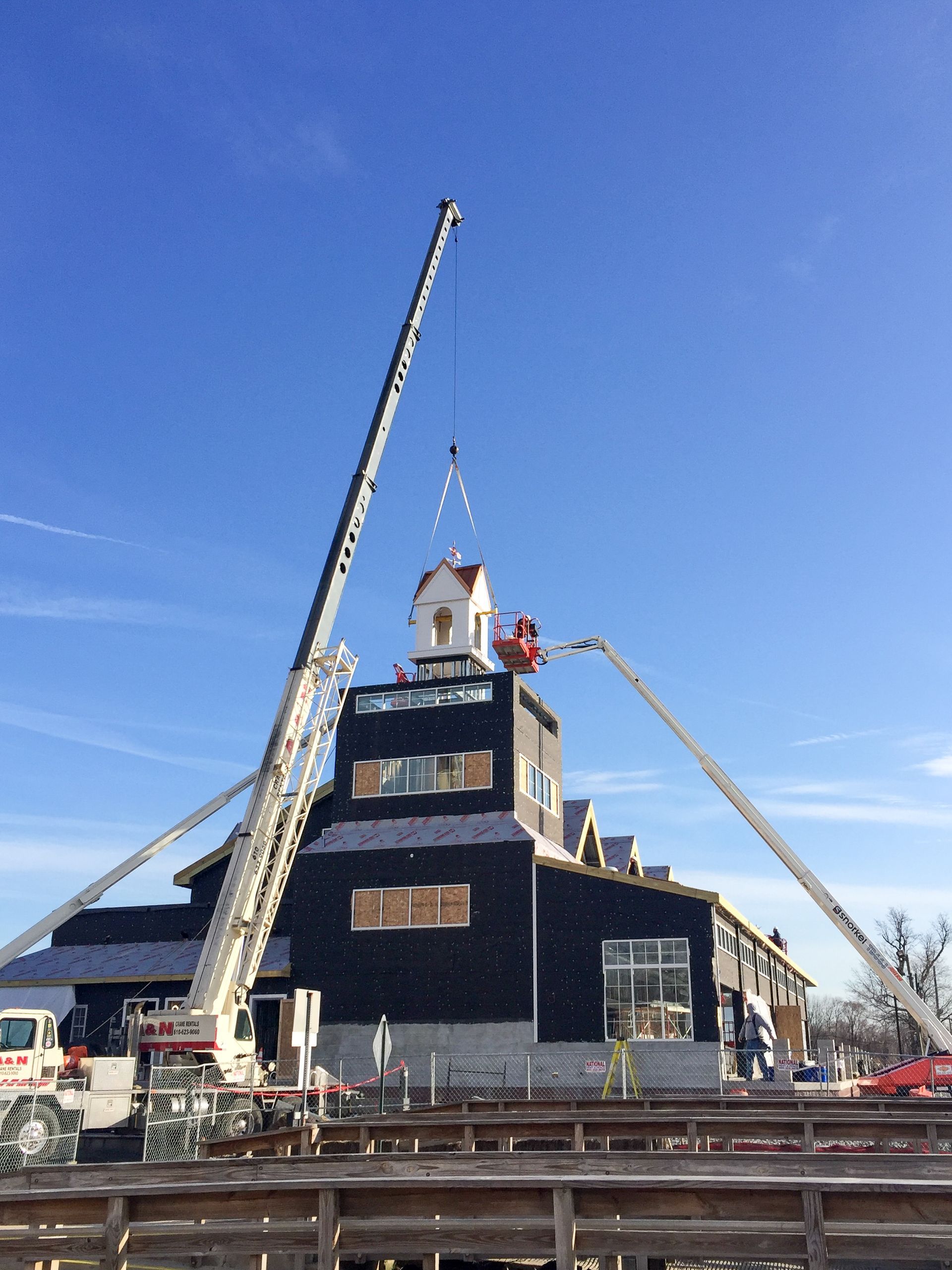 A white crane from A&N Crane Rental is lifting a a large piece of a roof and placing it on top of a building