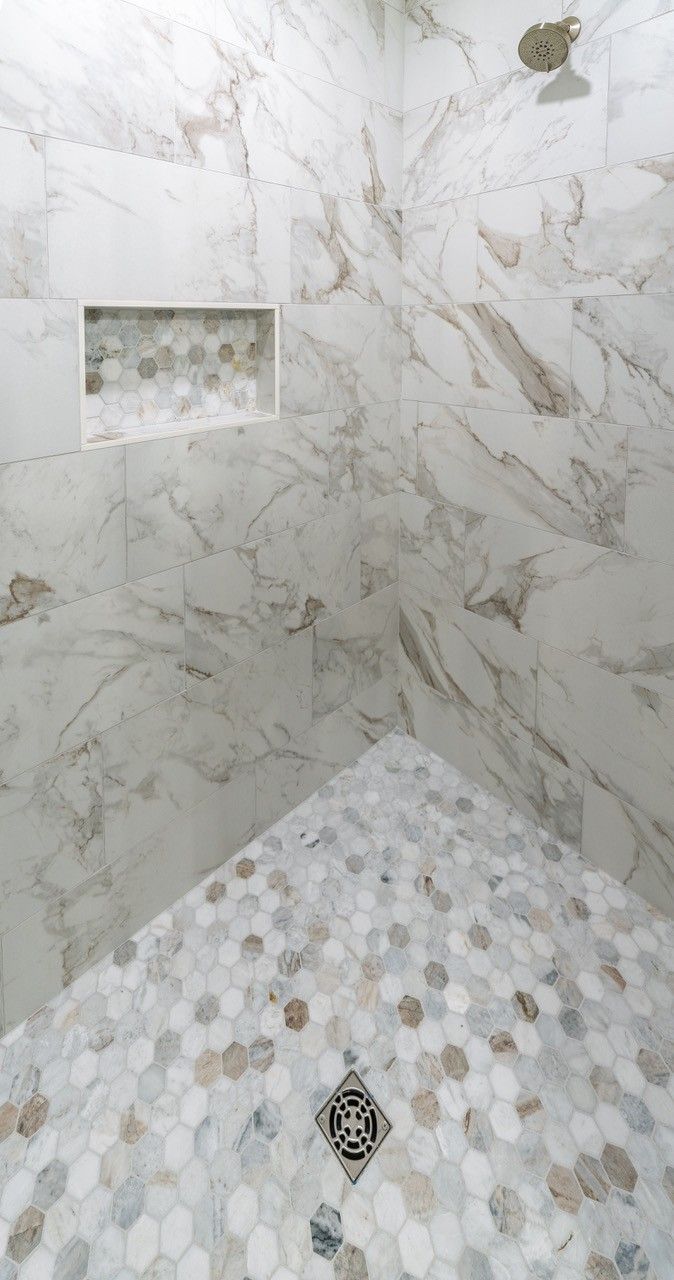 Bathroom with white marble tile walls and hexagonal mosaic floor in shower.