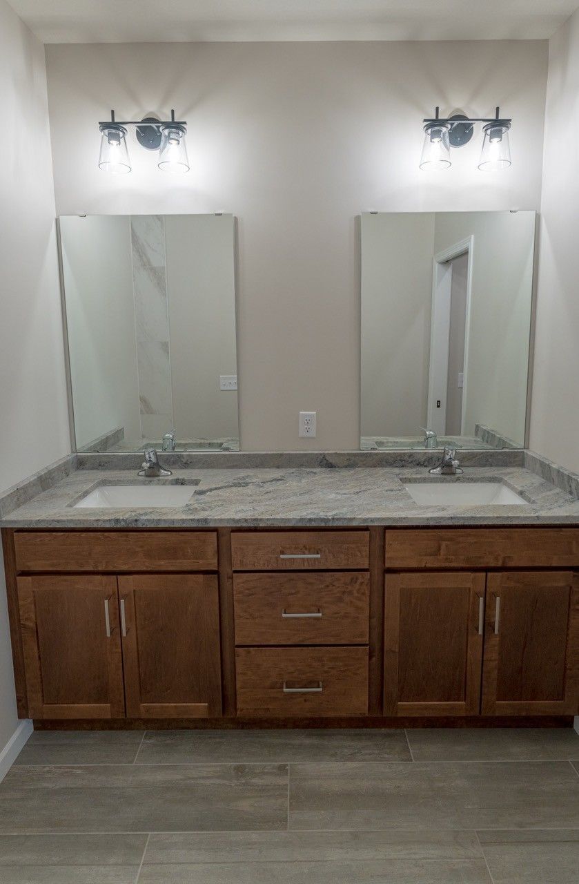 Bathroom with dual sinks, mirrors, and cabinetry; featuring granite countertop and sconce lighting.