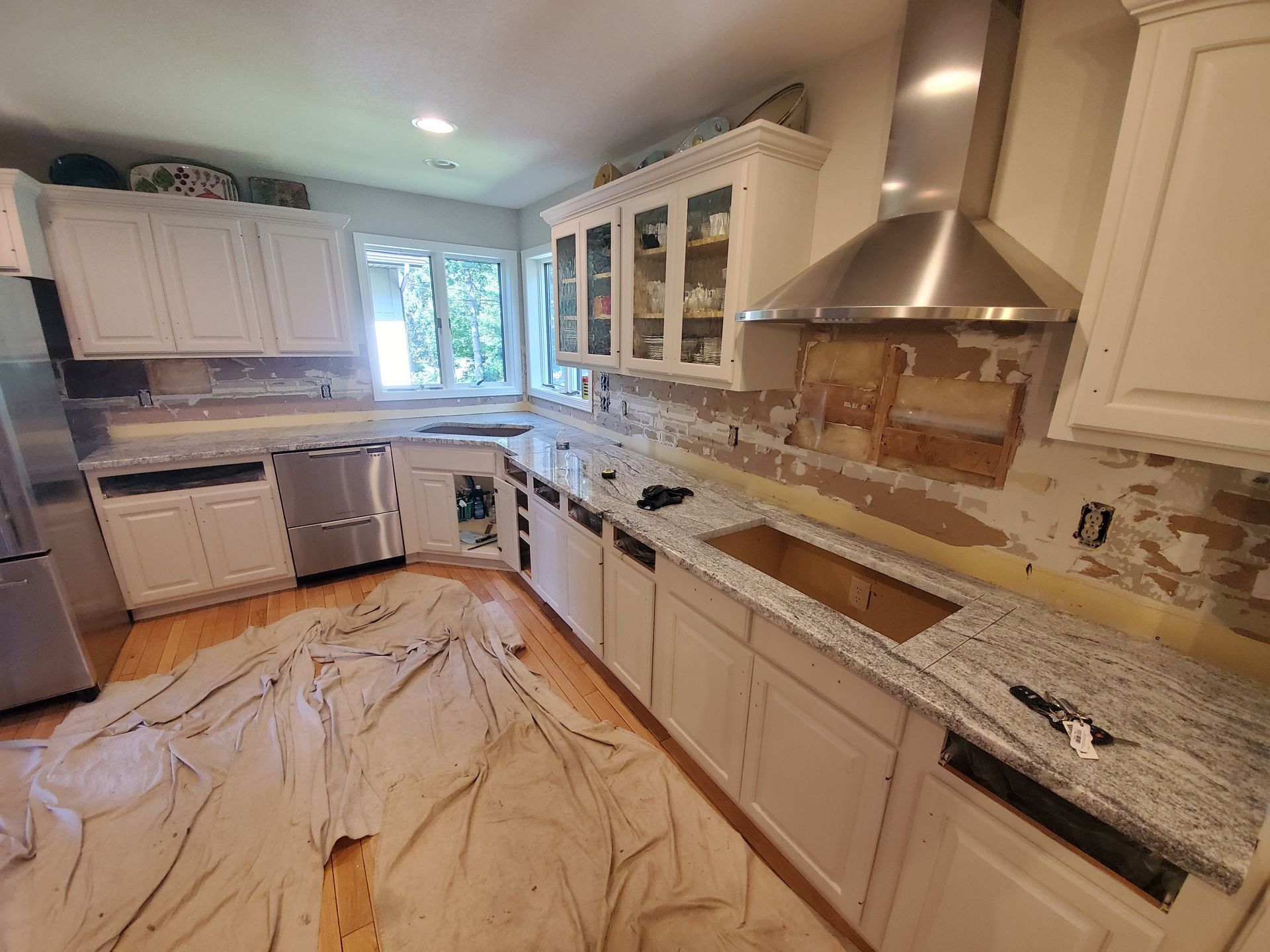 Kitchen under renovation with cabinets, countertops, and floor covered by protective drop cloths