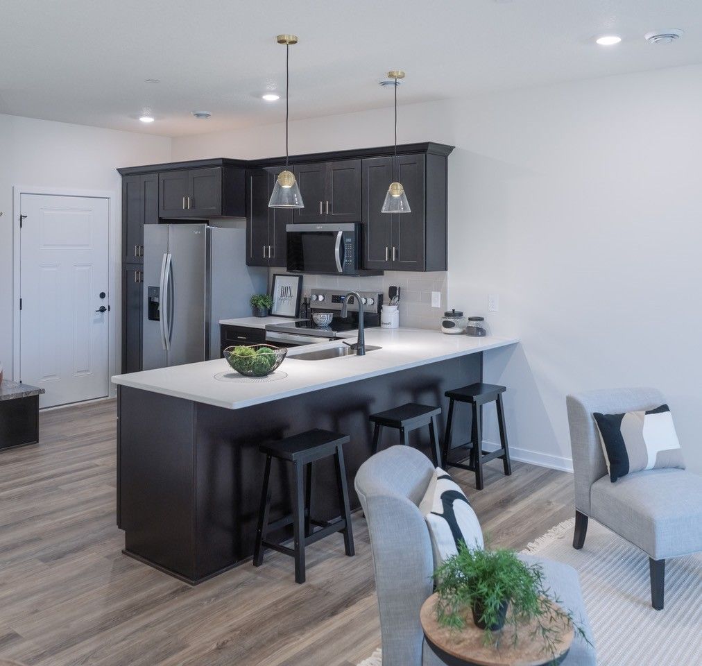 Modern kitchen with dark cabinets, white countertops, stainless steel appliances, and a breakfast bar with stools.