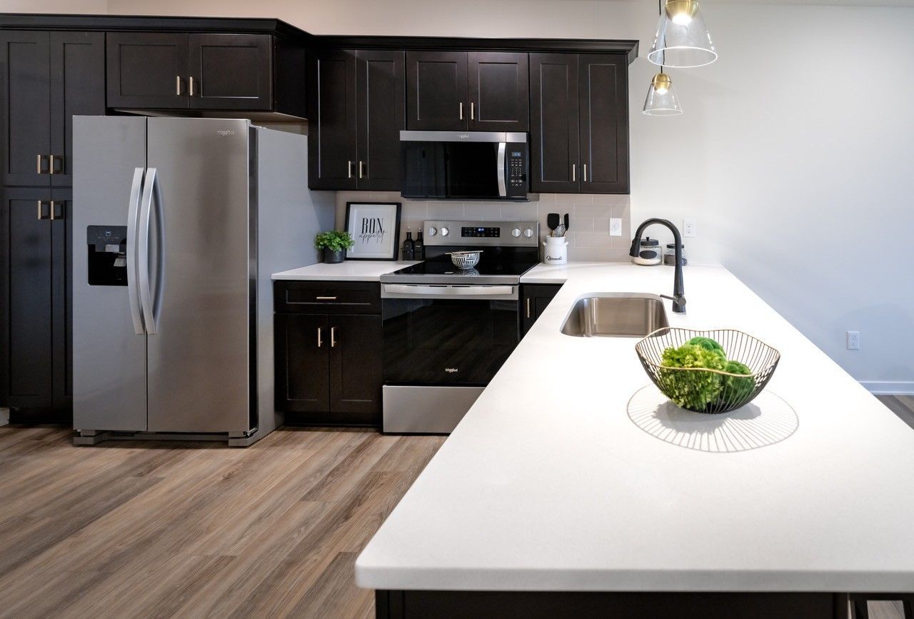 Modern kitchen with dark cabinets, stainless steel appliances, and a white countertop island.