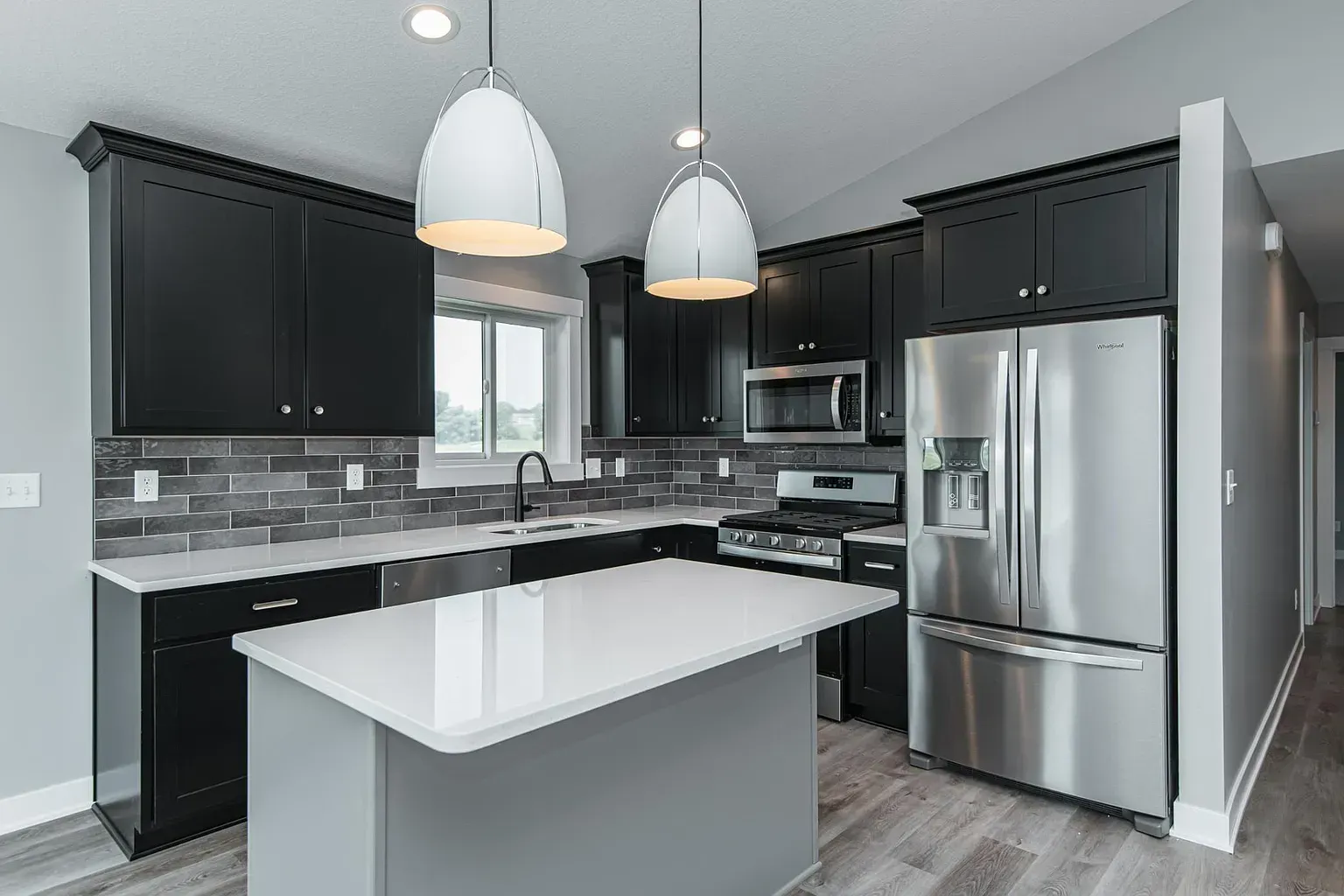 A kitchen with black cabinets , stainless steel appliances , and a large island.