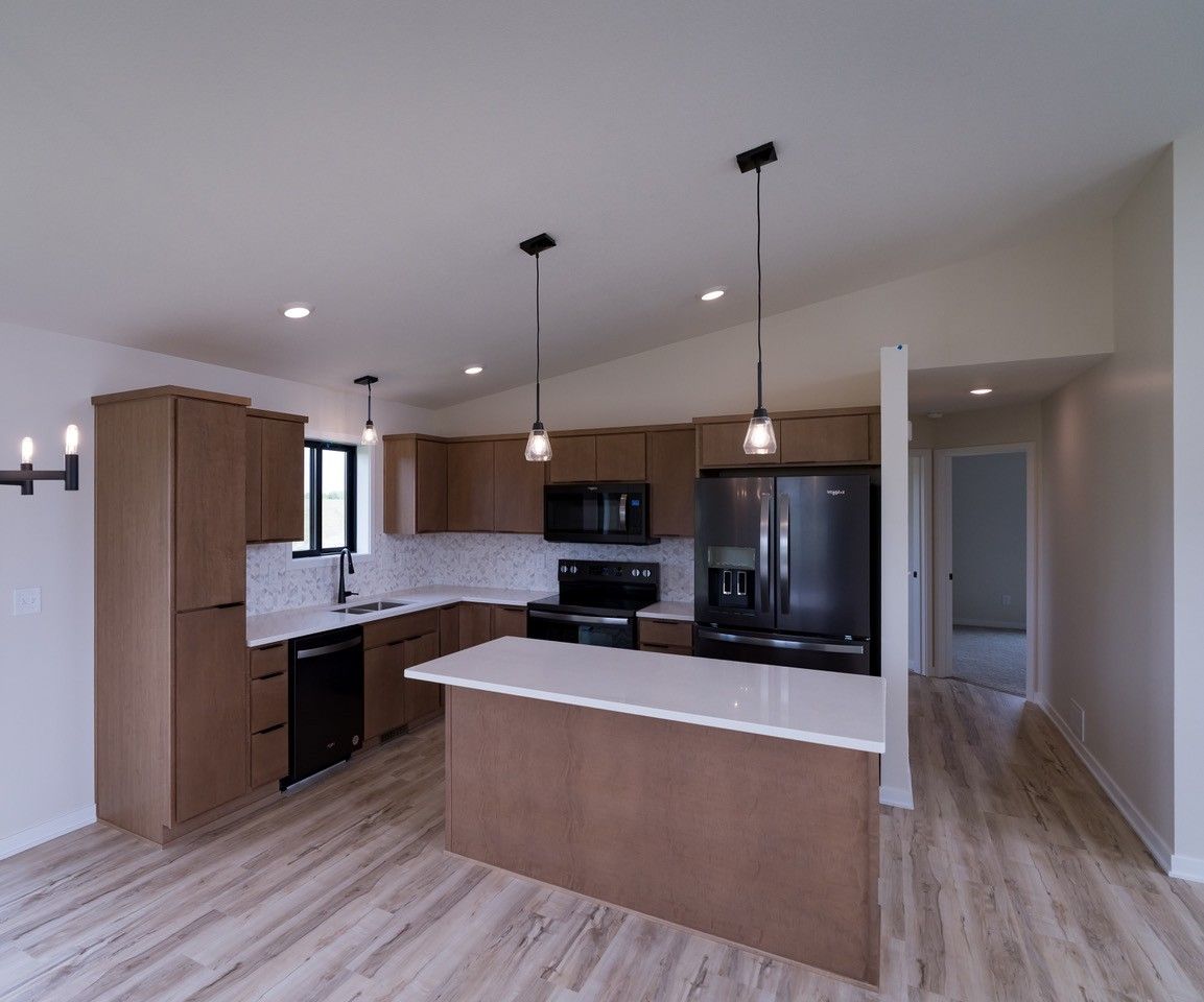 Modern kitchen with brown cabinets, white countertops, black appliances, and pendant lights.