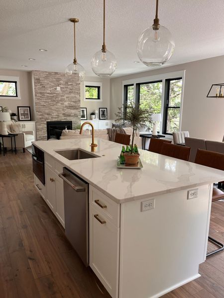White kitchen island with gold faucet and pendant lights, looking towards living area.