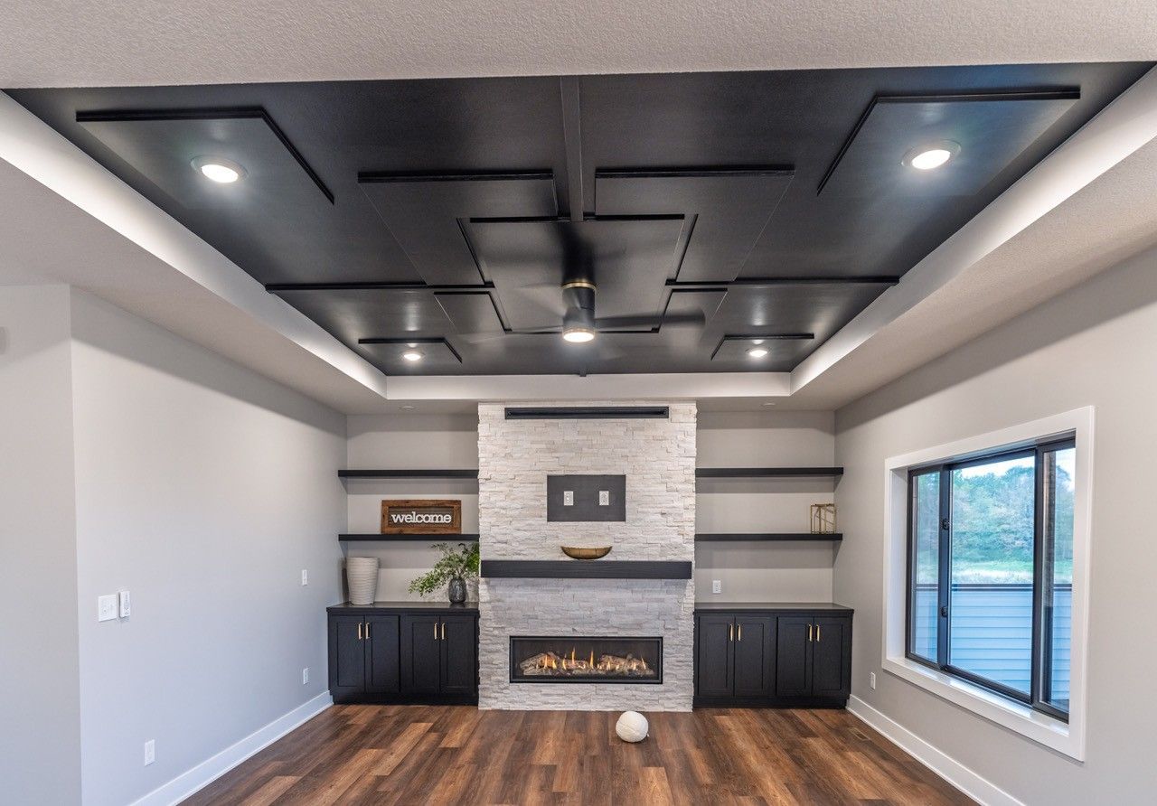 Modern living room with black ceiling accents, fireplace, shelves, and wood floors.