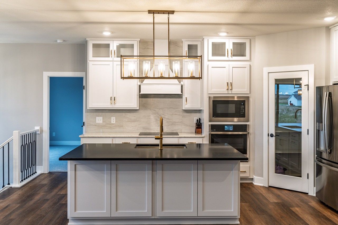 Modern kitchen with white cabinets, black island, and gold light fixture.