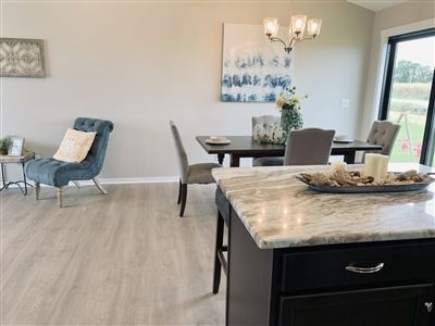 Open-concept dining and living area; blue armchair, dark dining table, light wood floors, and kitchen island.