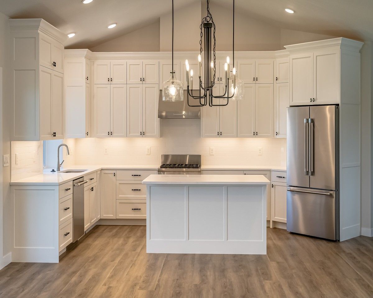 White kitchen with cabinets, island, stainless steel refrigerator and chandelier.