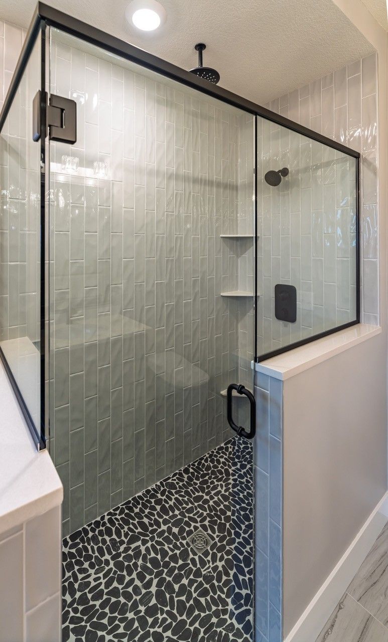 Glass shower with black frame, pebble floor, and white shelves.