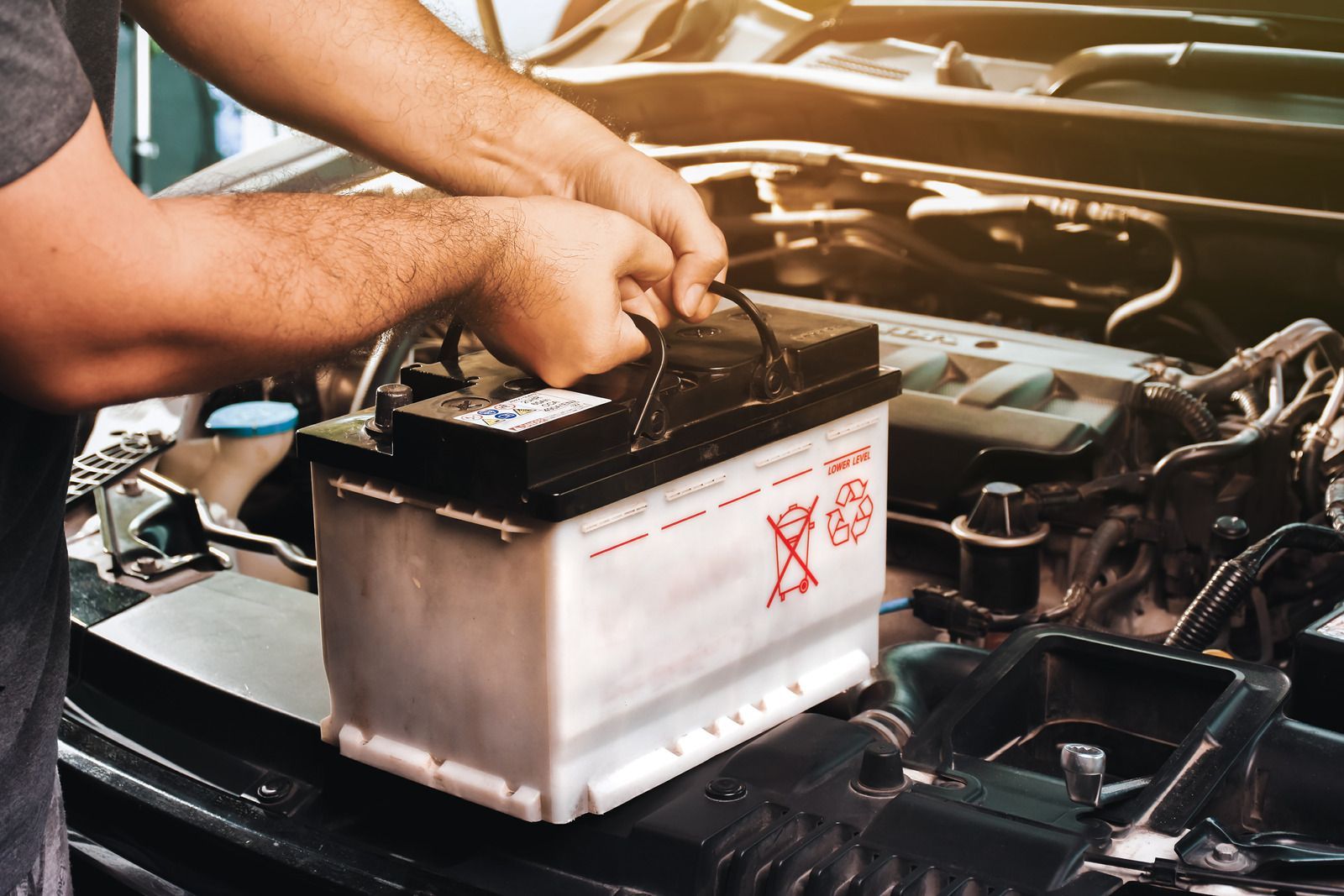 A man is changing a car battery in a garage.