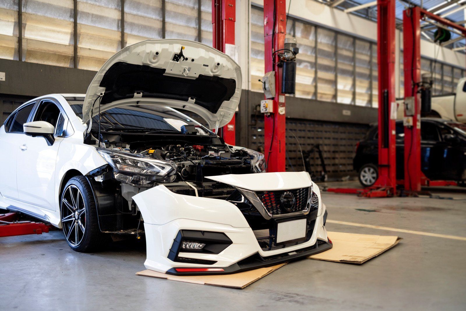 A white car is being repaired in a garage with the hood open.
