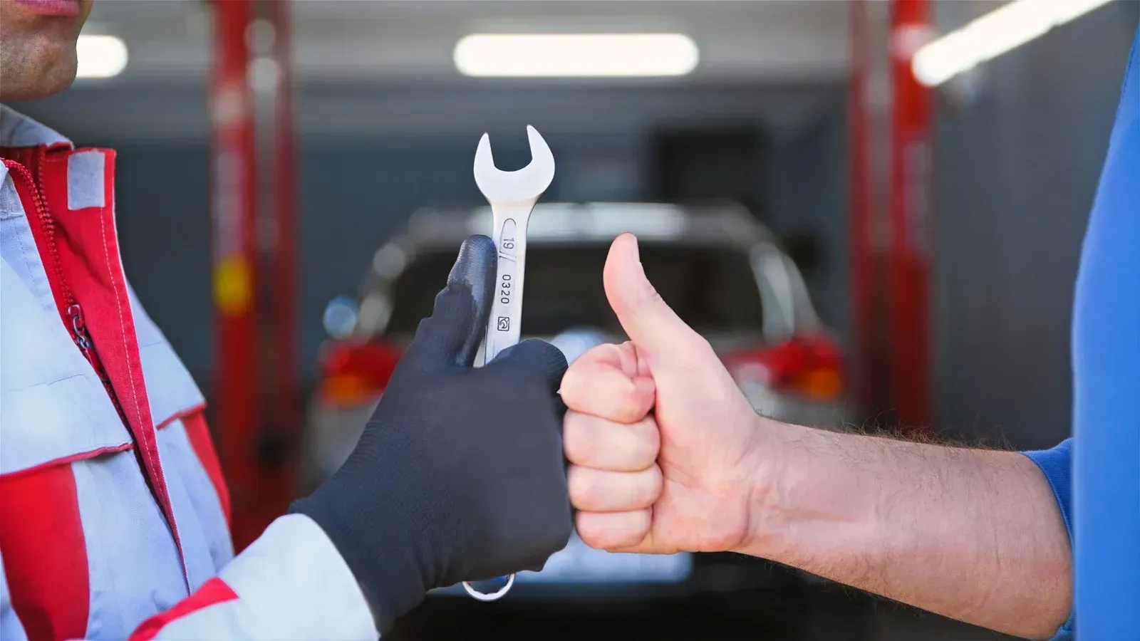 A man is giving a thumbs up while holding a wrench.