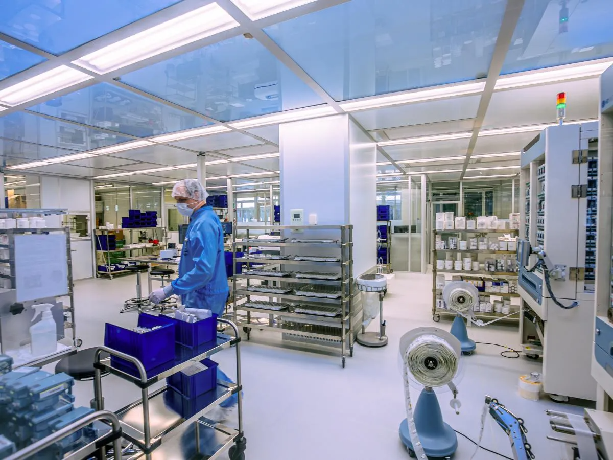 Eine Person in einem blauen Laboranzug arbeitet in einem Reinraum, umgeben von Geräten und Materialien.